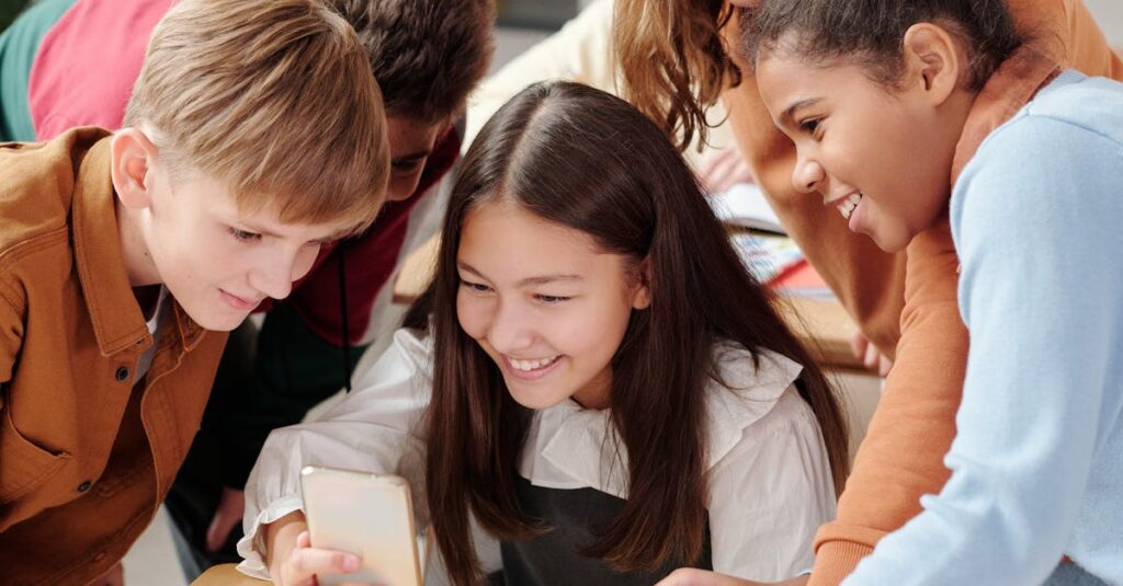 Happy students gathered around a smartphone in a lively classroom setting.